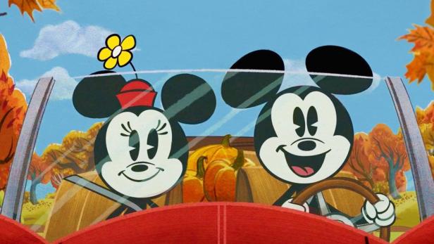 Micky und Minnie Maus fahren in einem roten Auto durch eine herbstliche Landschaft.