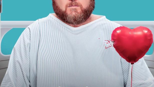 Ein Mann im Krankenhausbett hält einen roten Herzluftballon.