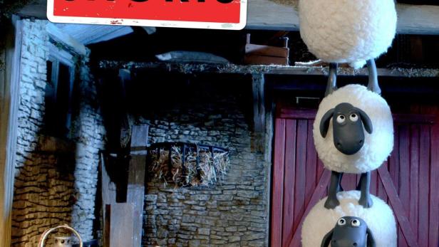 Schafe bilden einen Turm vor dem Hintergrund des Posters „Shaun das Schaf: Mossy Bottom Shorts“.