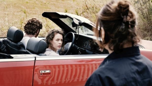 Paula Beer sitzt in einer Filmszene auf dem Beifahrersitz eines offenen roten Wagens.