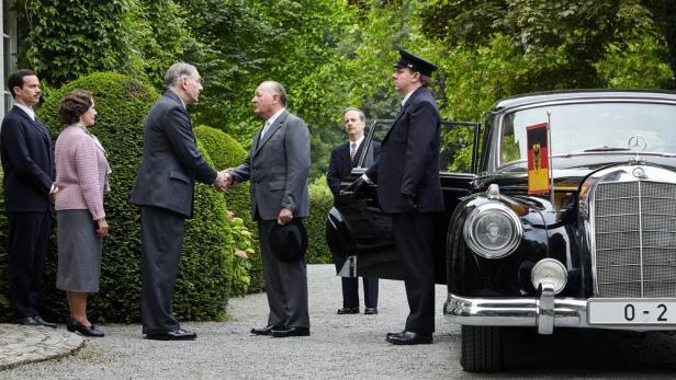 Burghart Klaußner als Bundeskanzler Konrad Adenauer begrüßt Jean-Yves Berteloot als Charles de Gaulle mit Handdruck vor einem Auto.