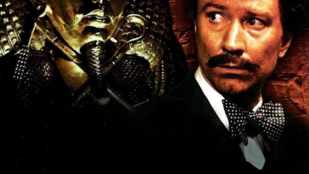 Ein Mann mit Fliege neben einer goldenen Tutanchamun-Maske, im Hintergrund das Filmplakat „Der Fluch des Tutanchamun“.