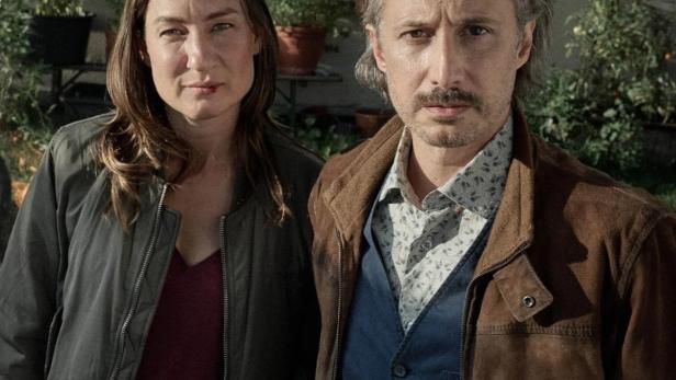 Eine Frau und ein Mann stehen vor einer Hauswand mit Pflanzenkübeln.