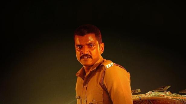 Ein Polizist steht vor einem goldenen Schirm mit Porträts für den Film „Vazha: Story of a Bangle“.