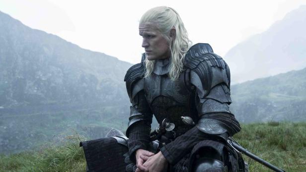 Matt Smith sitzt als Daemon Targaryen nachdenklich vor einer Naturkulisse.