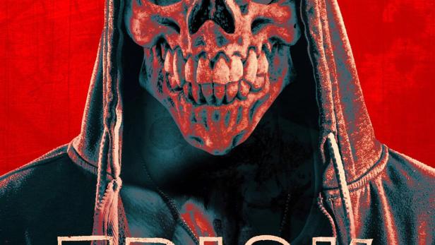 Ein Mann mit einer Totenkopfmaske und Kapuzenpullover vor einem roten Hintergrund.