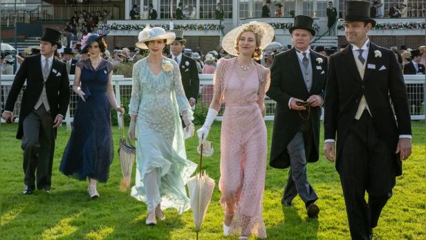 Hauptfiguren aus „Downton Abbey“ spazieren über einen Rasen.