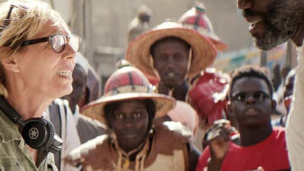 Eine Frau mit Kopfhörern spricht mit einer Gruppe von Menschen in traditioneller Kleidung.
