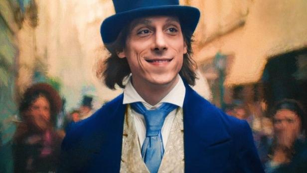 Ein Mann im Frack und Zylinder lächelt vor dem Hintergrund einer belebten Straße.