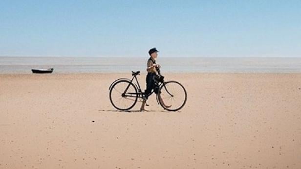 ein Junge mit Fahrrad am Strand.