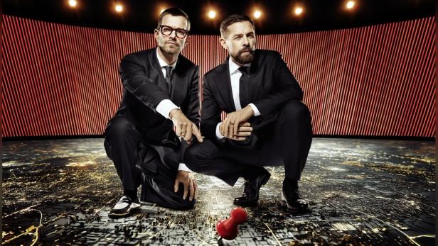 Joko Winterscheidt und Klaas Heufer-Umlauf kauern auf einem Studioboden, der das Satellitenbild einer Stadt zeigt.