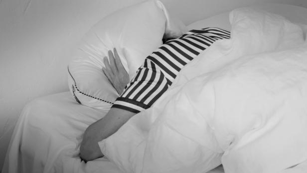 Frau liegt im Bett und hält sich mit beiden Händen das Kissen über den Kopf.