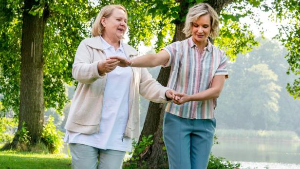 Mutter und Tochter halten einander vor Uferlandschaft  an den Händen