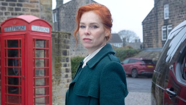 Rothaarige Frau steht vor einer britischen Telefonzelle