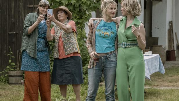Vier Frauen stehen reend und fotografierend in einem Gartren