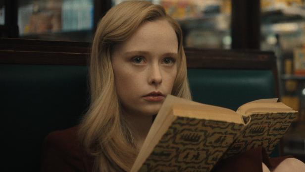 Junge Frau sitzt mit aufgeschlagenem Buch in einem Restaurant