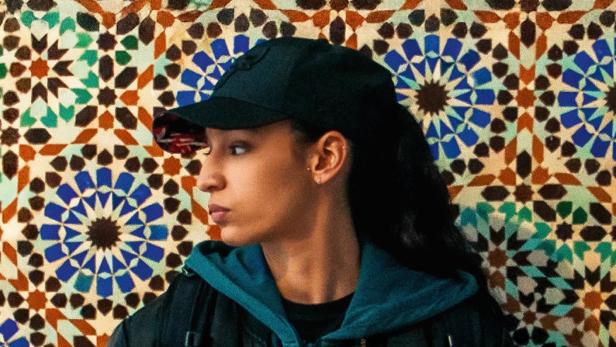 Mädchen steht vor bunt verzierter Wand und wendet und das Profil zu