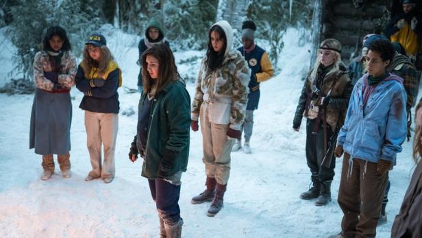 Junge Serienfiguren stehen im Schee vor einer Holzhütte im Wald