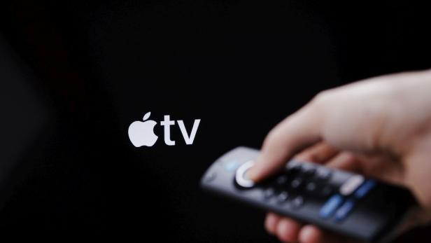 Apple TV Logo weiß auf schwarzem Hintergrund - im Vordergrund Hand mit Fernbedienung