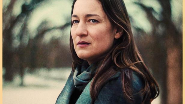 Frau steht mit verschränkten Armen vor kahlen Bäumen