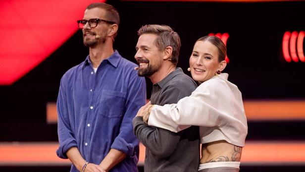 Mann wird von Frau in TV-Sendung von hinten umarmt