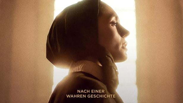 Frau in Kopftuch vor durchbrochenem Steinfenster