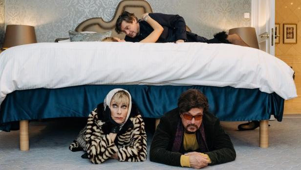 Mann und Frau verstecken sich unter einem Bett, während ein Paar darauf liegt