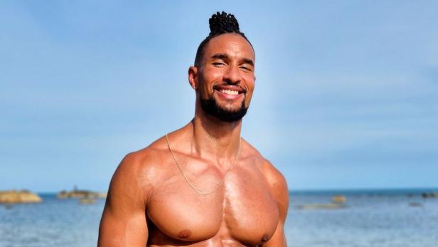 Mann mit muskulösem nackten Oberkörper vor Meereskulisse