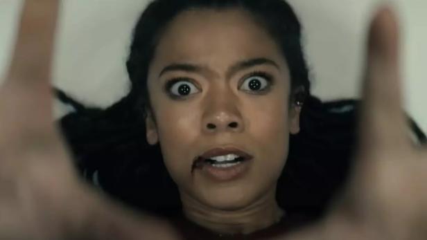 Großaufnahme von Jaz Sinclair in ihrer Rolle als Marie Moreau: sie liegt mit aufgerissenen Augen am Boden und streckt beide Hände in die Höhe