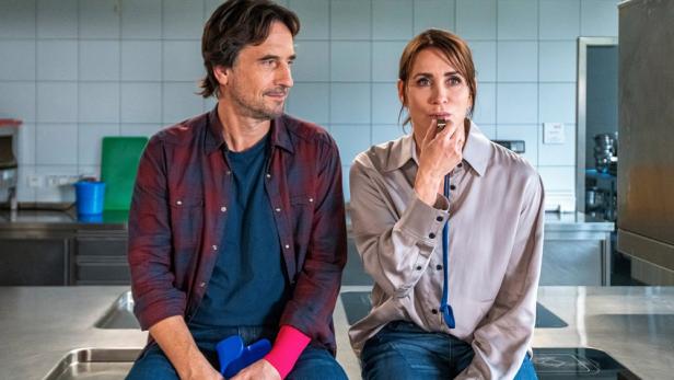 Mann und Frau sitzen in einer Küche auf Arbeitsfläche nebeneinander