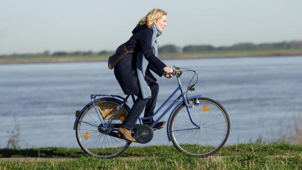 Frau fährt auf Fahrrad an Flussufer entlang