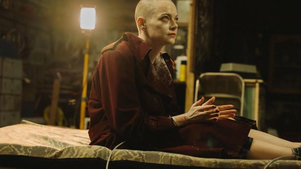 Kahlgeschorene Frau sitzt in Keller auf einer Liege