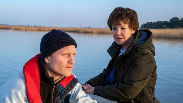 Frau unterhält sich an Meeresarm mit Mann - im Hintergrund sieht man Schilf