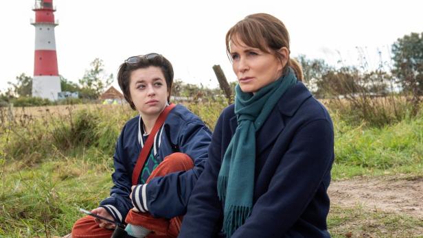 Zwei Frauen sitzen in den Dünen bei einem Leuchtturm