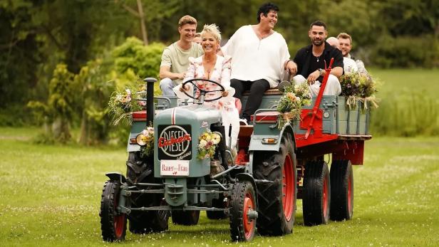 Inka Bause lenkt Traktor mit Anhänger, auf dem Bauern sitzen