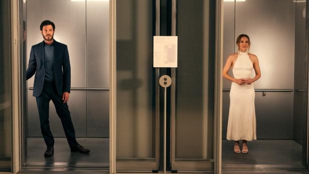Mann und Frau stehen in zwei nebeneinanderliegenden Aufzugskabinen