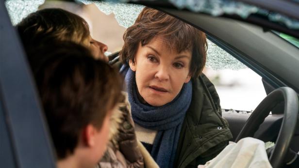 Frau beugt sich in Auto, dessen Scheiben zerbrochen sind, zu Beifahreren