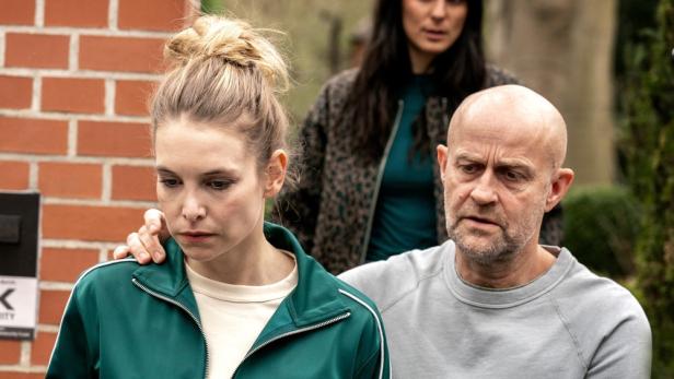 Frau wird von Mann geführt, der ihr die Hand auf die Schulter legt