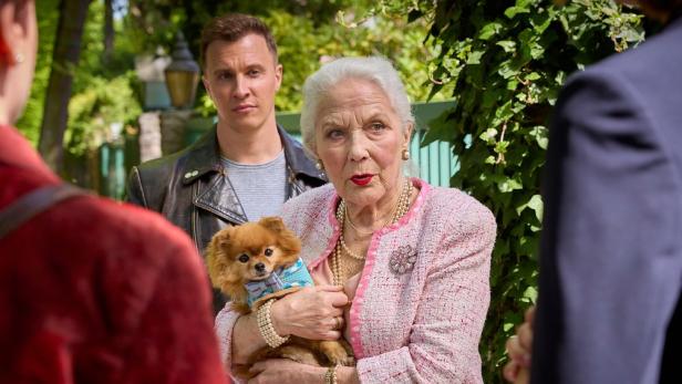 Böse blickende ältere Frau hält einen kleinen Hund beschützend im Arm