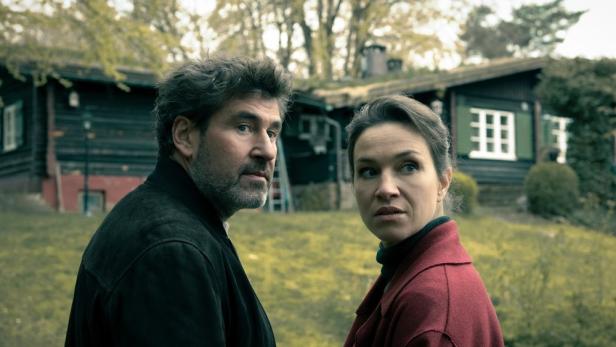 Mann und Frau stehen auf der Wiese im Garten vor zwei grünen Holzhäusern 