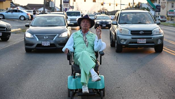 Mann sitzt auf Parkplatz in einem Rollator