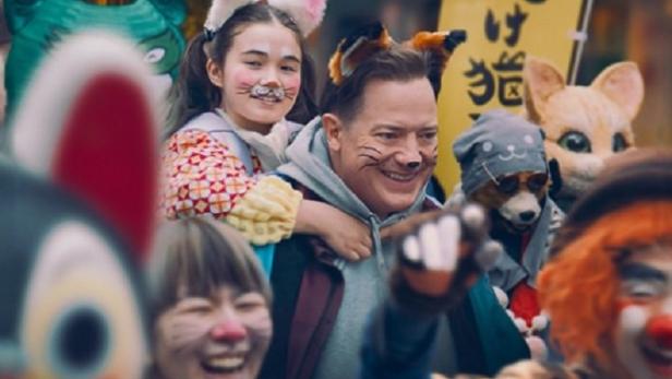 Als Katze geschminkter Mann trägt ein ebenso maskiertes Kind auf dem Rücken