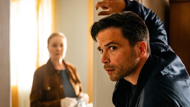 Mann stützt sich auf einen Türstock, während im Hintergrund der Wohnung eine Frau steht