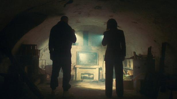 Zwei Personen leuchten mit Taschenlampen in einem dunklen Kellerartigen Raum auf eine Feuerstelle