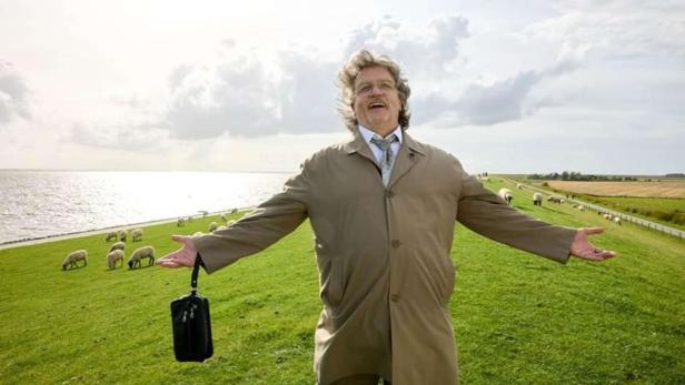 Hape Kerkeling steht als Horst Schlämmer mit ausgebreiteten Armen auf einer Schafwiese am Meer 