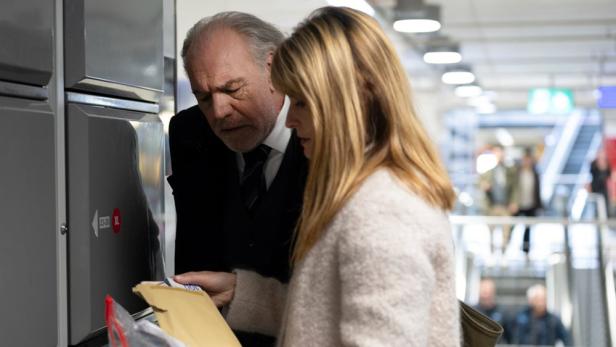 Mann und Frau beugen sich bei Bahnhofschließfach über Kuvert