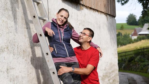 Mann hält Frau umfangen, die ein paar Sprossen hoch auf einer Leiter steht