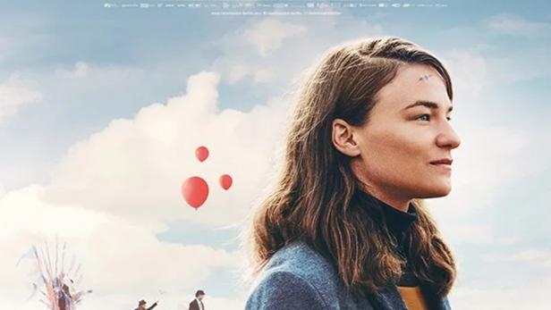 Frau mit genähter Wunde auf der Stirn blickt unter blauem Himmel in die Ferne