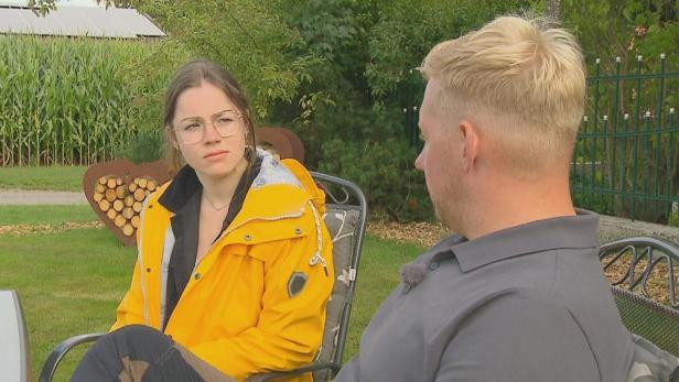 Frau sitzt Mann in einem Garten gegenüber und beide blicken einander an