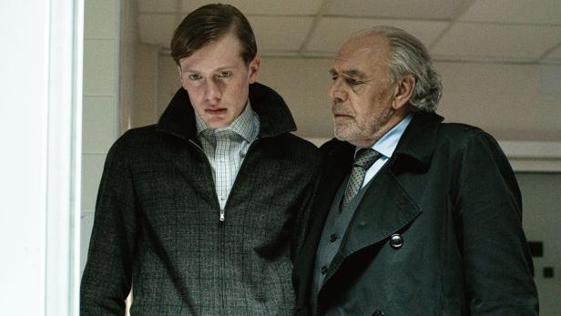 Junger Mann blickt auf etwas und wird von einem älteren dabei beobachtet